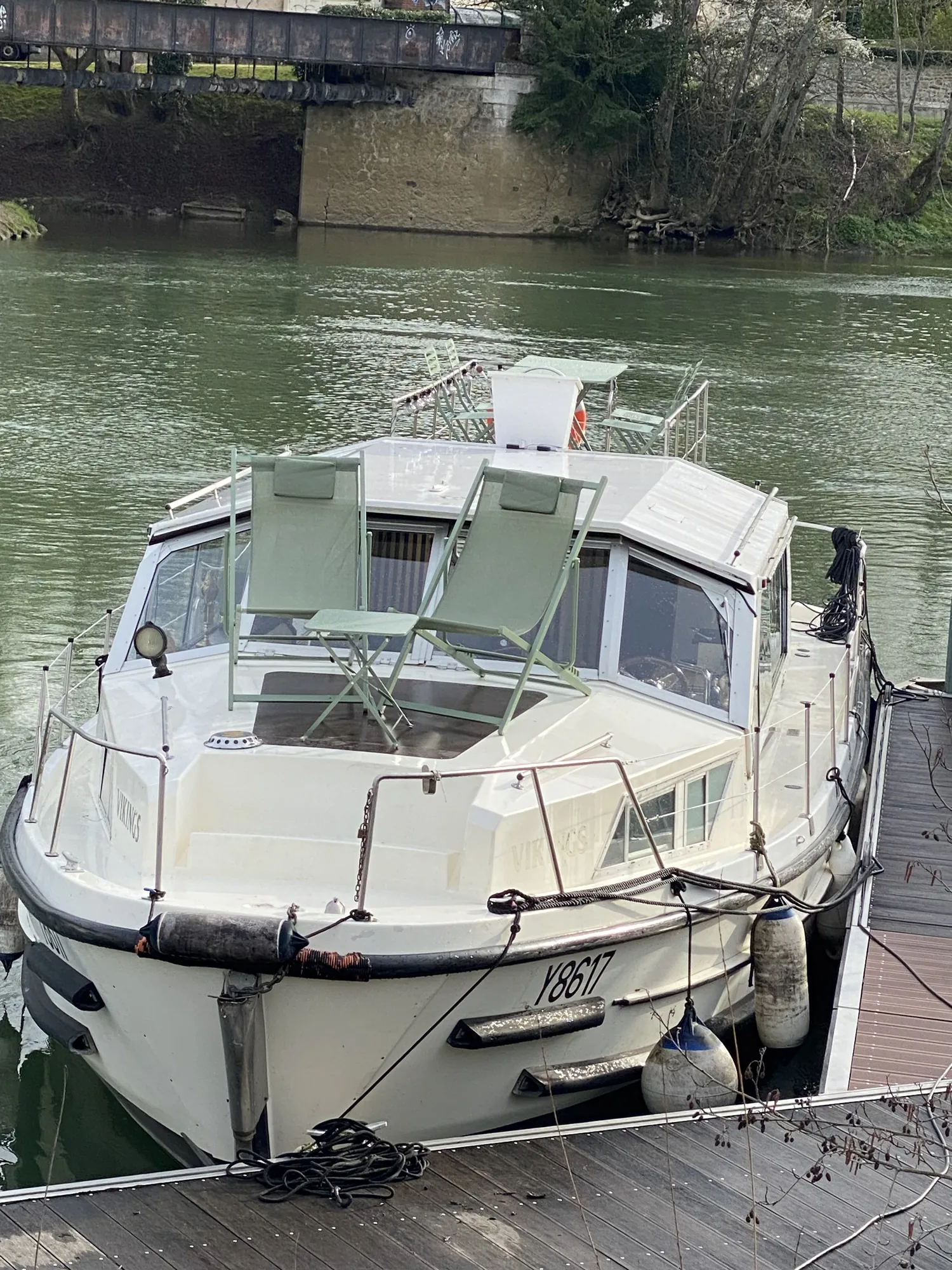 Table et chaises de bistrot vertes sur le pont d'un bateau amarré au bord de la Marne, dans l'esprit guinguette